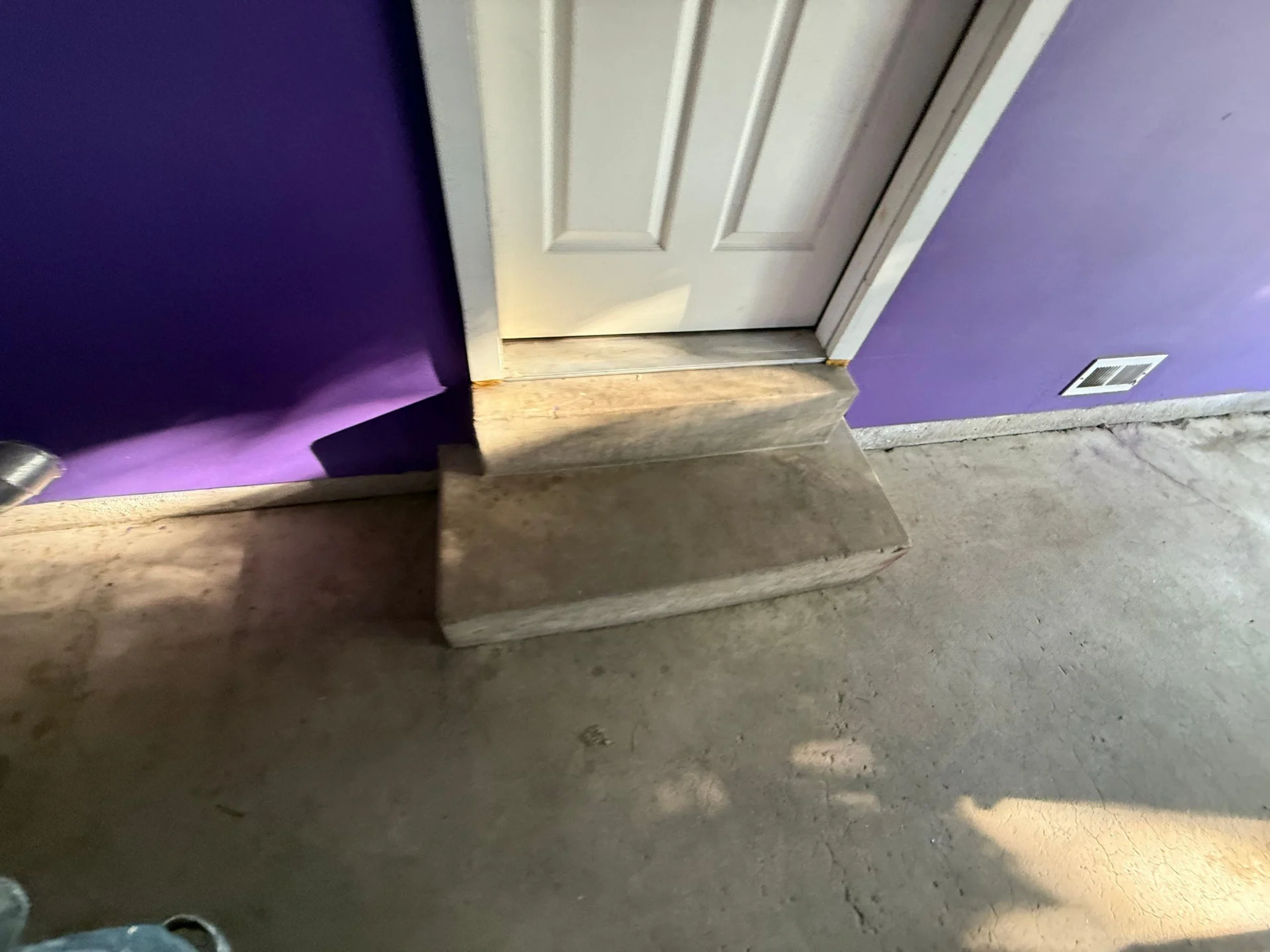 Concrete steps leading to a white door with purple walls.